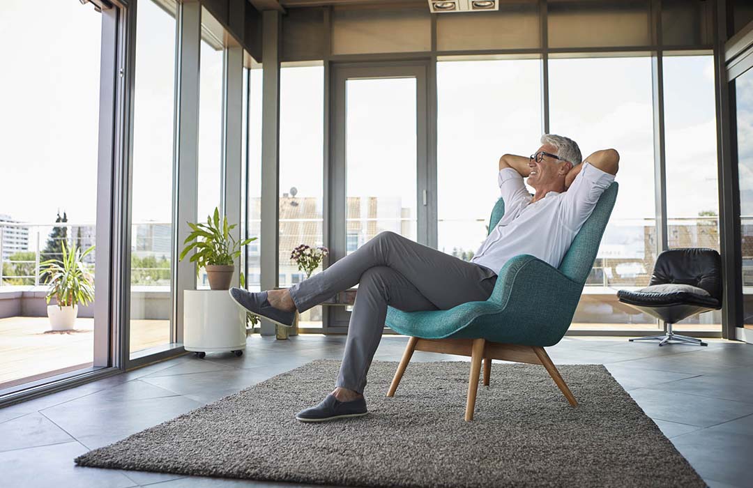 Smiling mature man relaxing in armchair at the window at home Peltier Financial